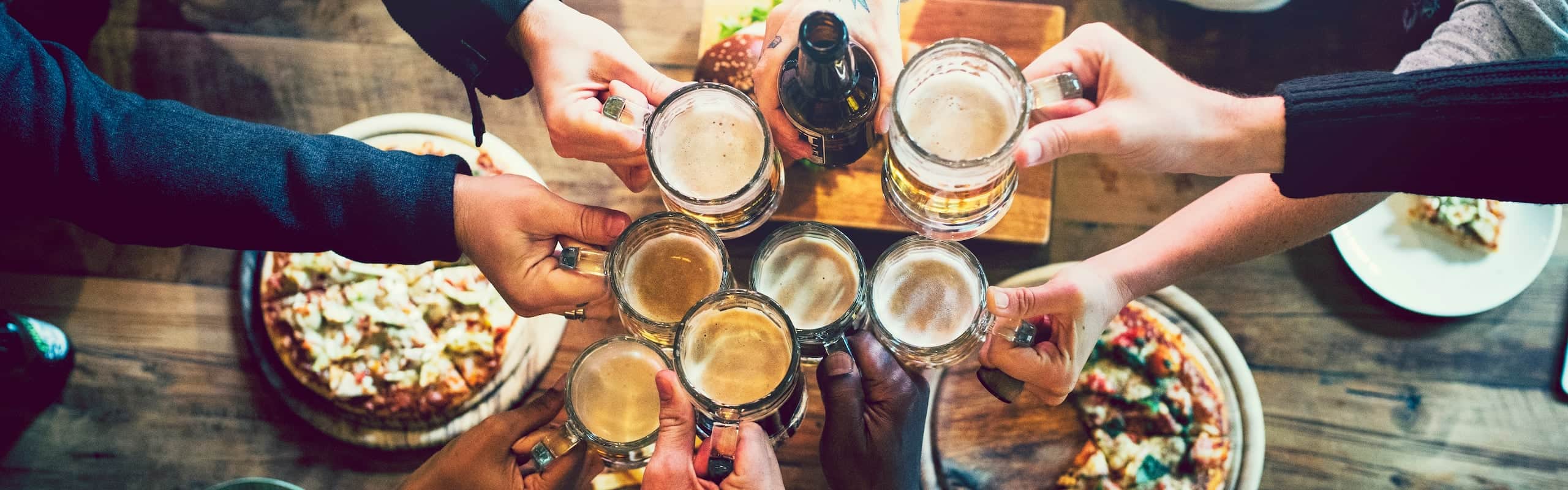 people are toasting their glasses of drink and some pizzas