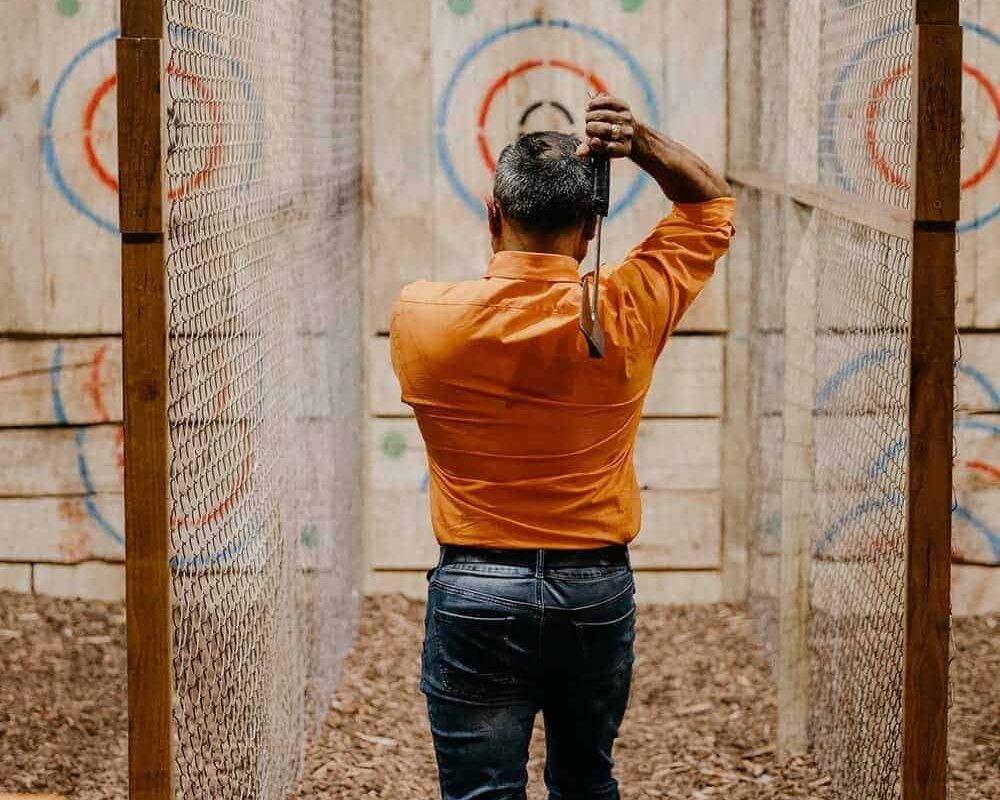a man in orange polo is enjoying the axe throwing at lumber punks