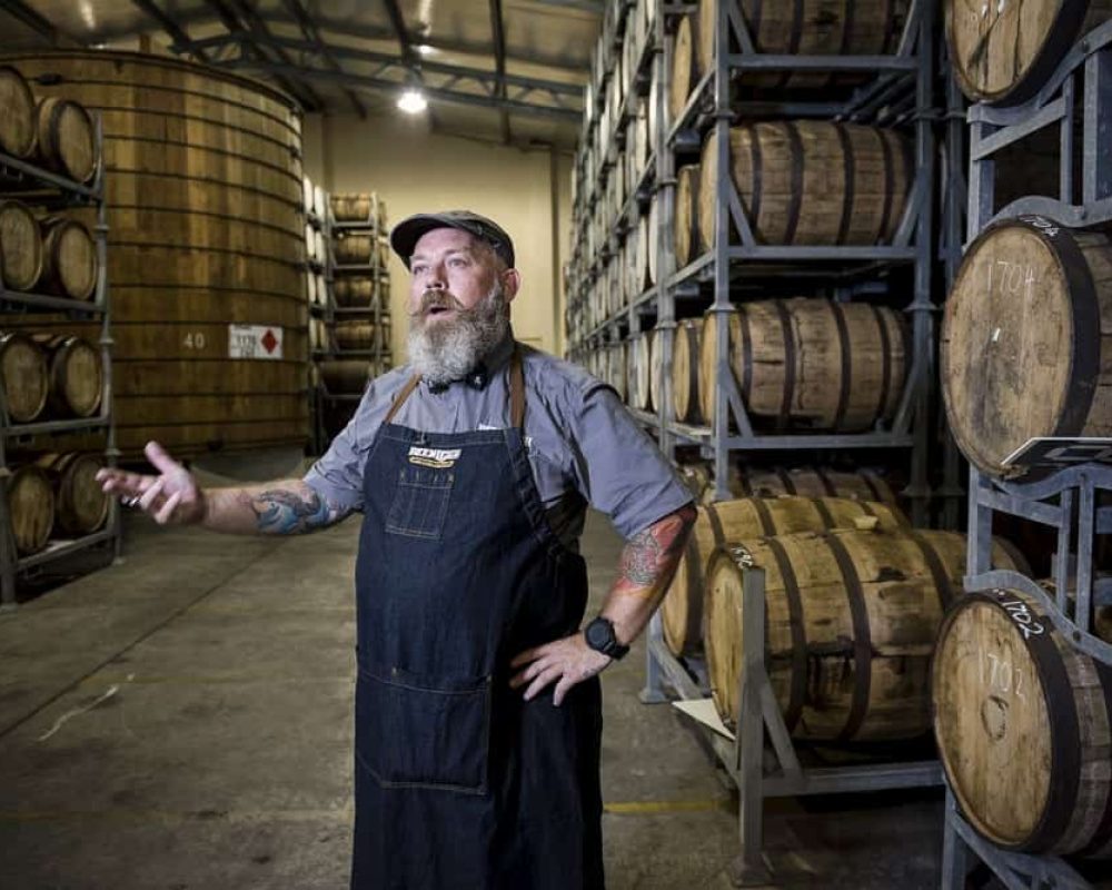 a man in an apron and a gray polo is inside an beer cellar